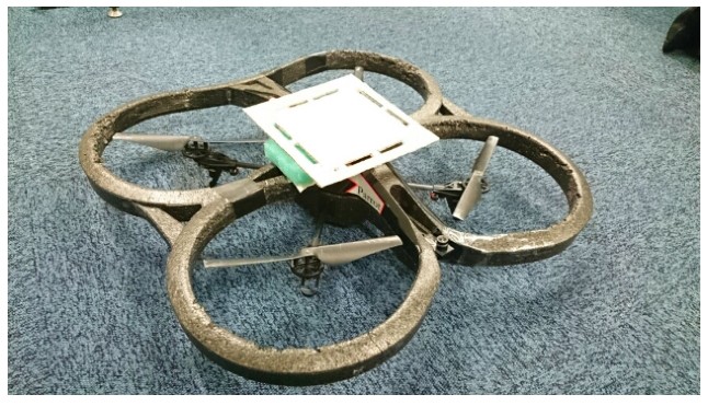 AR.Drone quadcopter with its protective hull and a flat white plate mounted on top.