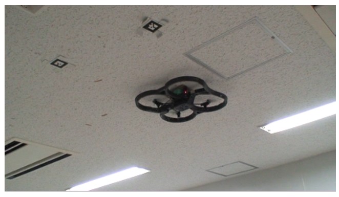 The drone seen from below, flying just under a ceiling with markers on it.
